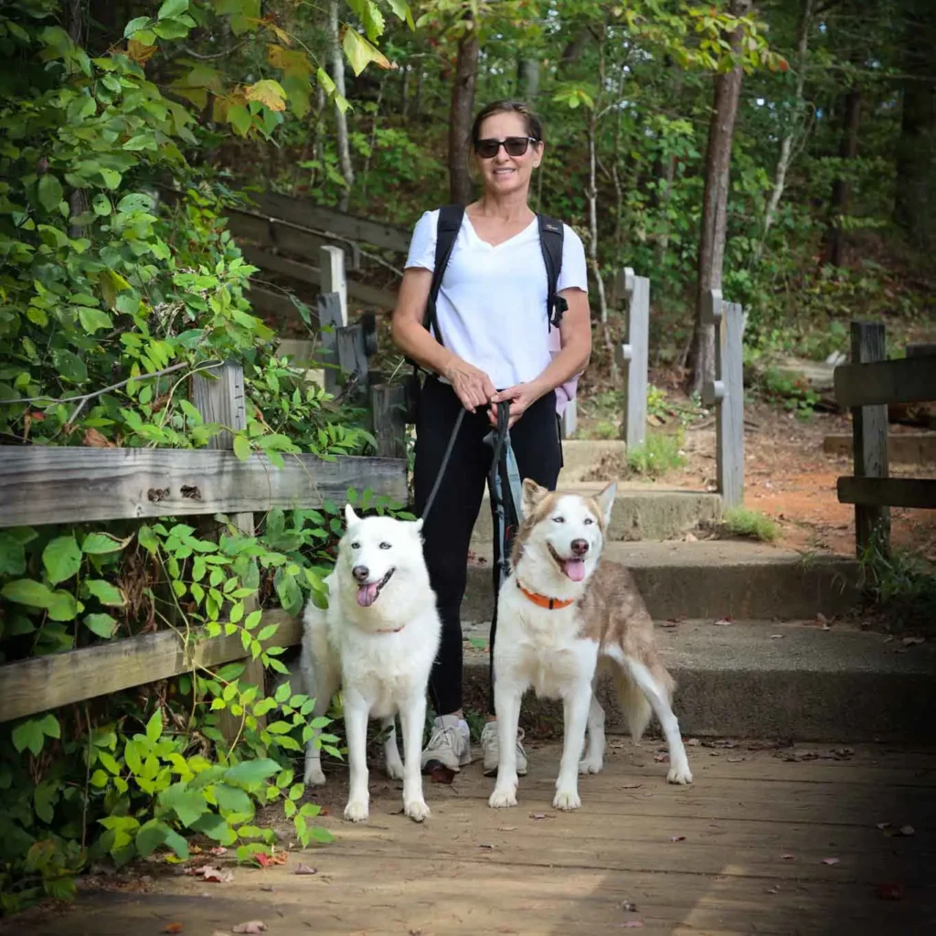 woman standing on a bridge with two huskies on the leash